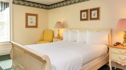 Hotel sleigh bed with floral wallpaper border, framed prints and a yellow armchair.
