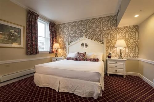 Hotel bedroom with king bed, patterned wallpaper and floral window curtains.