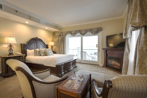 Lake view hotel room with seating area, fireplace and doors to a private balcony.
