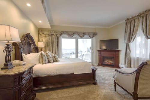 Lake view hotel room with carved wood bed, fireplace, television and balcony doors.