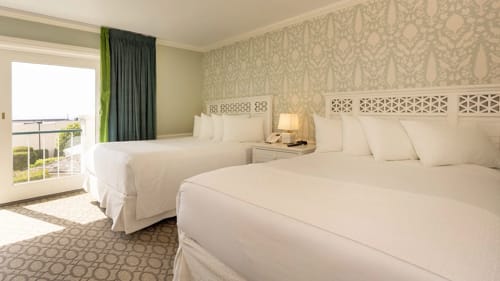 Hotel bedroom with two queen beds and a Juliet balcony overlooking the water.