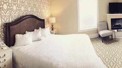 Hotel king bed with leather headboard beside a fireplace and television.