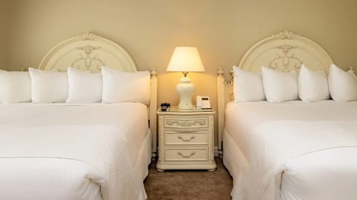 Two hotel beds with carved cream headboards sharing a lamp-topped nightstand.